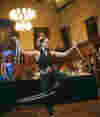 A performer dances and spins with silver hula hoops in a warmly lit room filled with paintings.