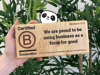 Hand holding a B Corp wooden plaque with The Cheeky Panda's logo peaking behind the plaque.