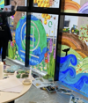 An artist paints on a large window, creating a colorful illustration that features the Earth and the B Corp Certification logo.