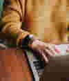 Person in a yellow jumper typing on a laptop on a wooden table