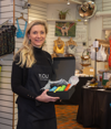 Sarah Jordan, founder of YOU Underwear holding a box of product at their physical store, with underwear displays in the background.