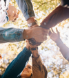 A group of people stand in a circle, stacking their hands together in a huddle, symbolising unity and collaboration across the B Corp community.
