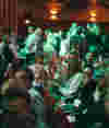 Audience crowd seated in the main stage theatre chatting to each other, with green lighting.